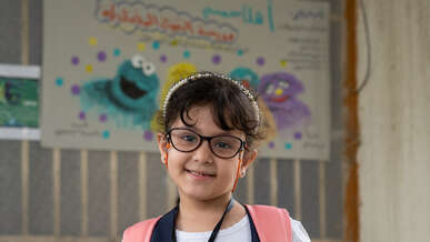 A girl in a classroom smiles and poses for a portrait.